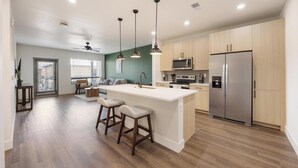 A modern kitchen with a central island, bar stools, a refrigerator, and a microwave. - Landing | Spectacular 1BD, Gym, Courtyard (Goodyear)
