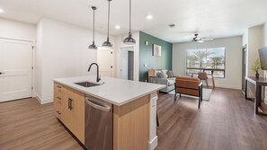 A modern kitchen with a built-in dishwasher, a dining area with a table and chairs, and a living room with a sofa and a coffee table. - Landing | Beautiful 2BD, Clubhouse, Game Room (Goodyear)