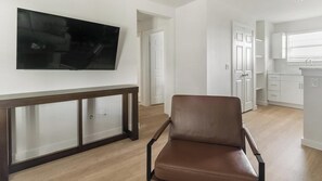 Un salon moderne avec un fauteuil en cuir marron, un téléviseur à écran plat fixé au mur et une console en bois.