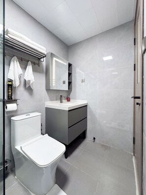 Un bagno moderno con toilette, lavandino e specchio. Asciugamani appesi a un porta-asciugamani e una cabina doccia con porta in vetro.