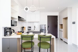 Una cocina moderna con armarios blancos, horno empotrado y refrigerador. Hay dos sillas verdes con un diseño único.