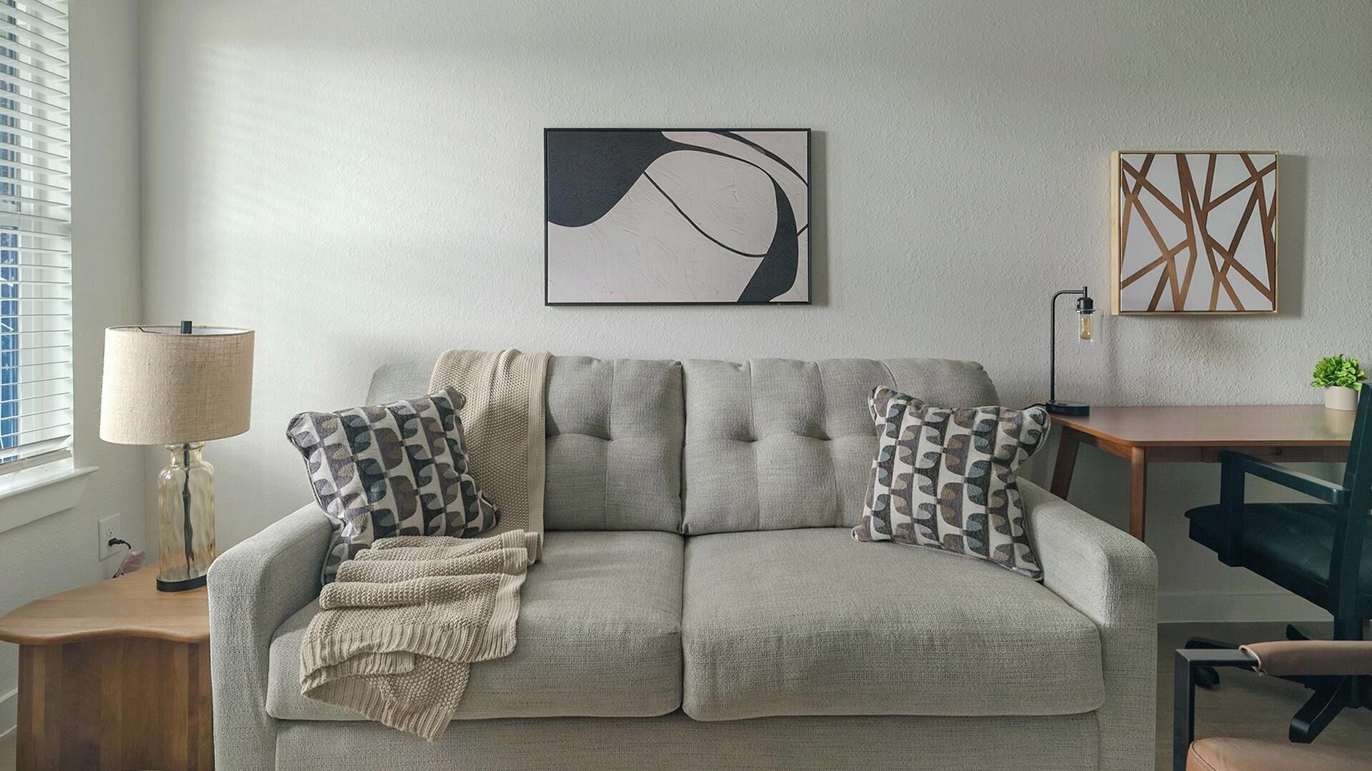 A neutral-toned sofa with patterned cushions, a lamp, and wall art in a well-lit room.