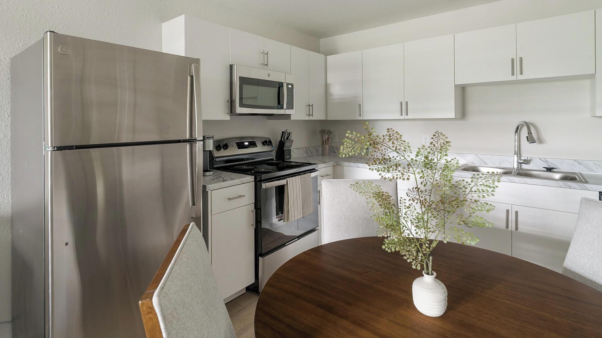 Une cuisine moderne dotée d’appareils électroménagers en acier inoxydable, de meubles blancs, d’un plan de travail en marbre et d’une table à manger agrémentée d’un vase de fleurs.