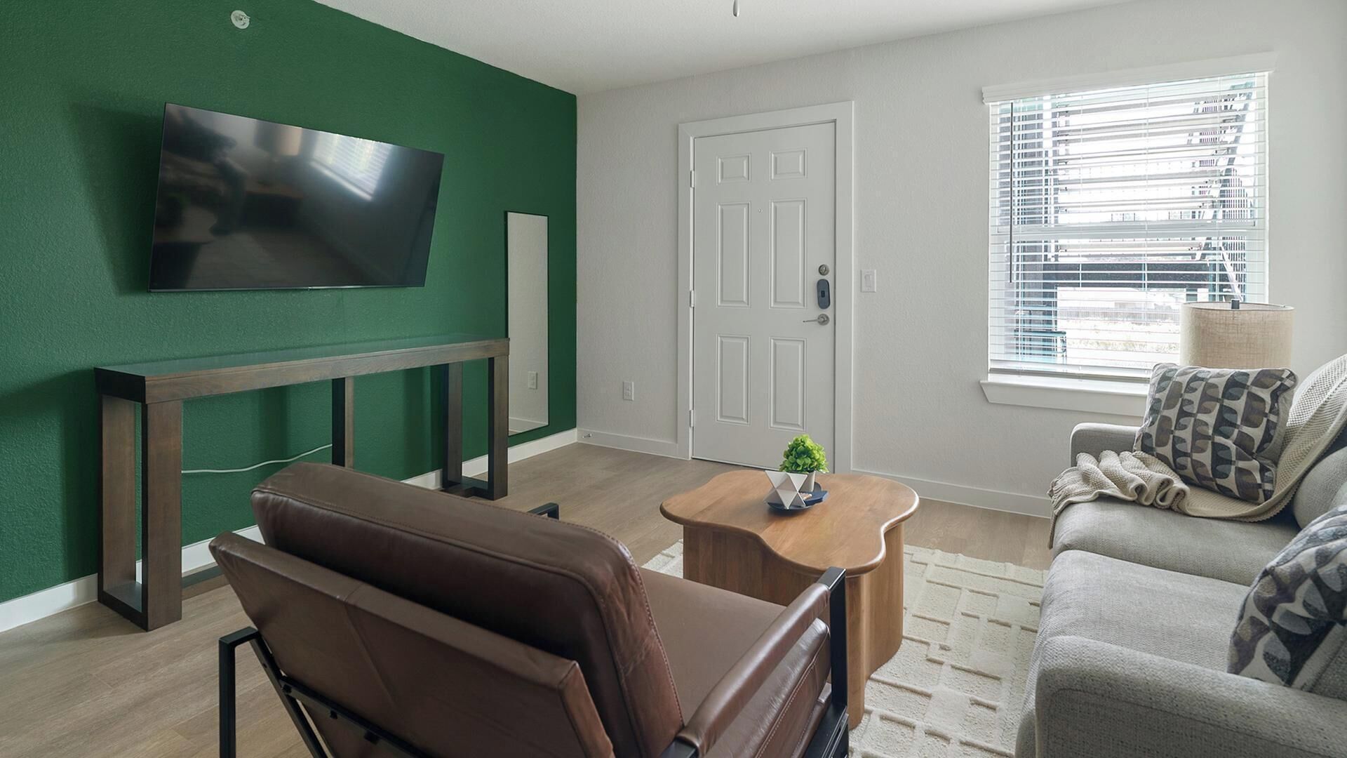 Ein Wohnzimmer mit Wand-Fernseher, braunem Ledersofa, einem Holztisch und einem grauen Sofa mit gemusterten Kissen.