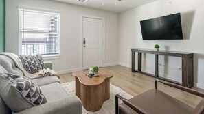Ein Wohnzimmer mit Sofa, Couchtisch, Fernseher und einer Tür.