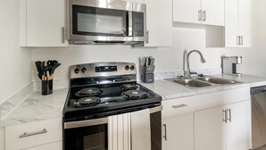 Une cuisine moderne équipée d’une cuisinière en acier inoxydable, d’un four à micro-ondes, d’un évier et de meubles de rangement blancs.