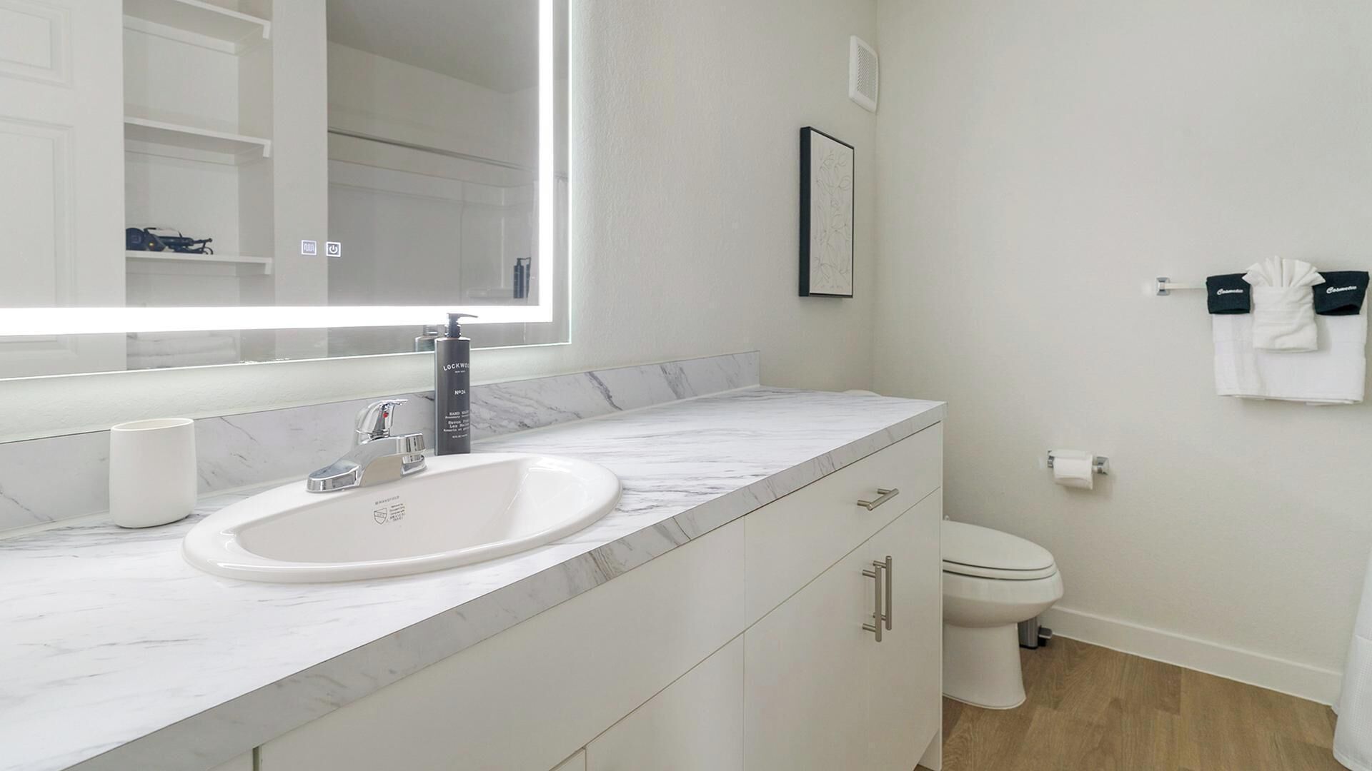A modern bathroom with a white sink, a large mirror, a toilet, and a cabinet.