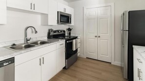 A modern kitchen with a dishwasher, double sink, stove, microwave, and a refrigerator. - Landing | Chic 1BD in Bear Creek (Houston)