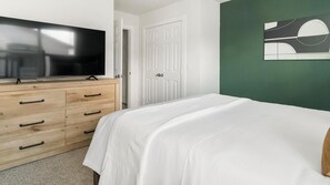 A bedroom with a bed, a dresser, a television, and a door. - Landing | Chic 1BD in Bear Creek (Houston)