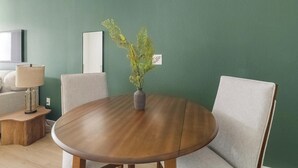 Ein runder Holztisch mit Blumen in einer Vase, zwei Stühle, eine Lampe und ein Spiegel an der Wand.