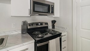 A kitchen with a stainless steel stove, a microwave above it, and a sink with a faucet. - Landing | Modern 1BD in Bear Creek (Houston)