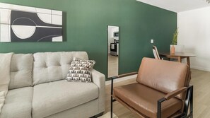 A modern living room with a green accent wall, a sofa, a brown leather chair, and a minimalist artwork. - Landing | Stunning 1BD in Bear Creek (Houston)