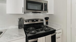 A kitchen with a stainless steel stove, a microwave, and a set of knives. - Landing | Stunning 1BD in Bear Creek (Houston)