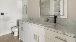A modern bathroom with a marble countertop, a sink, a toilet, and a mirror. - Landing | Stunning 1BD in Bear Creek (Houston)