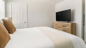 A bedroom with a bed, a television on a wooden dresser, and a white door. - Landing | Stunning 1BD in Bear Creek (Houston)