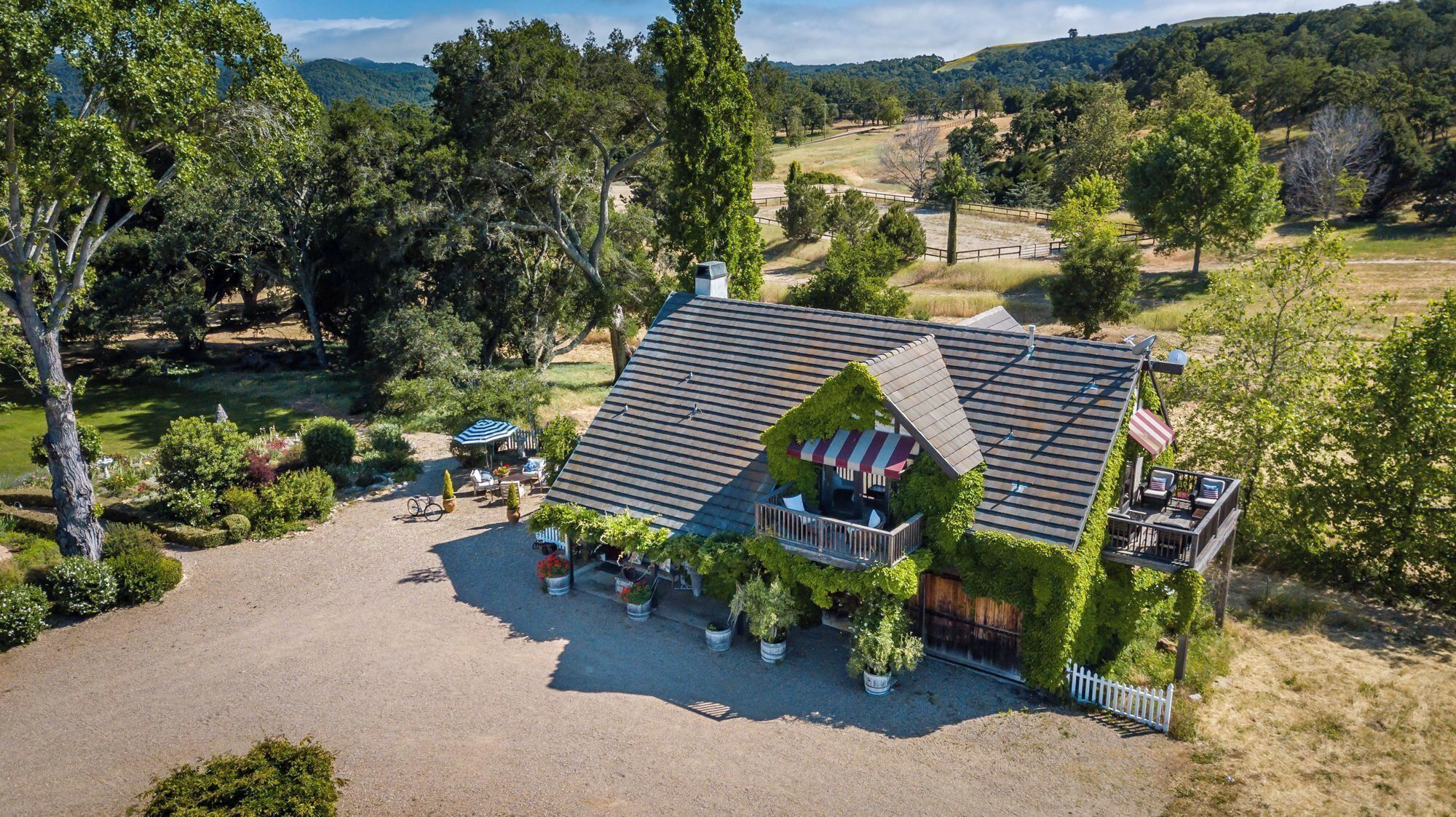 A house with a sloped roof, surrounded by a gravel driveway, and a fenced garden area with outdoor seating.
