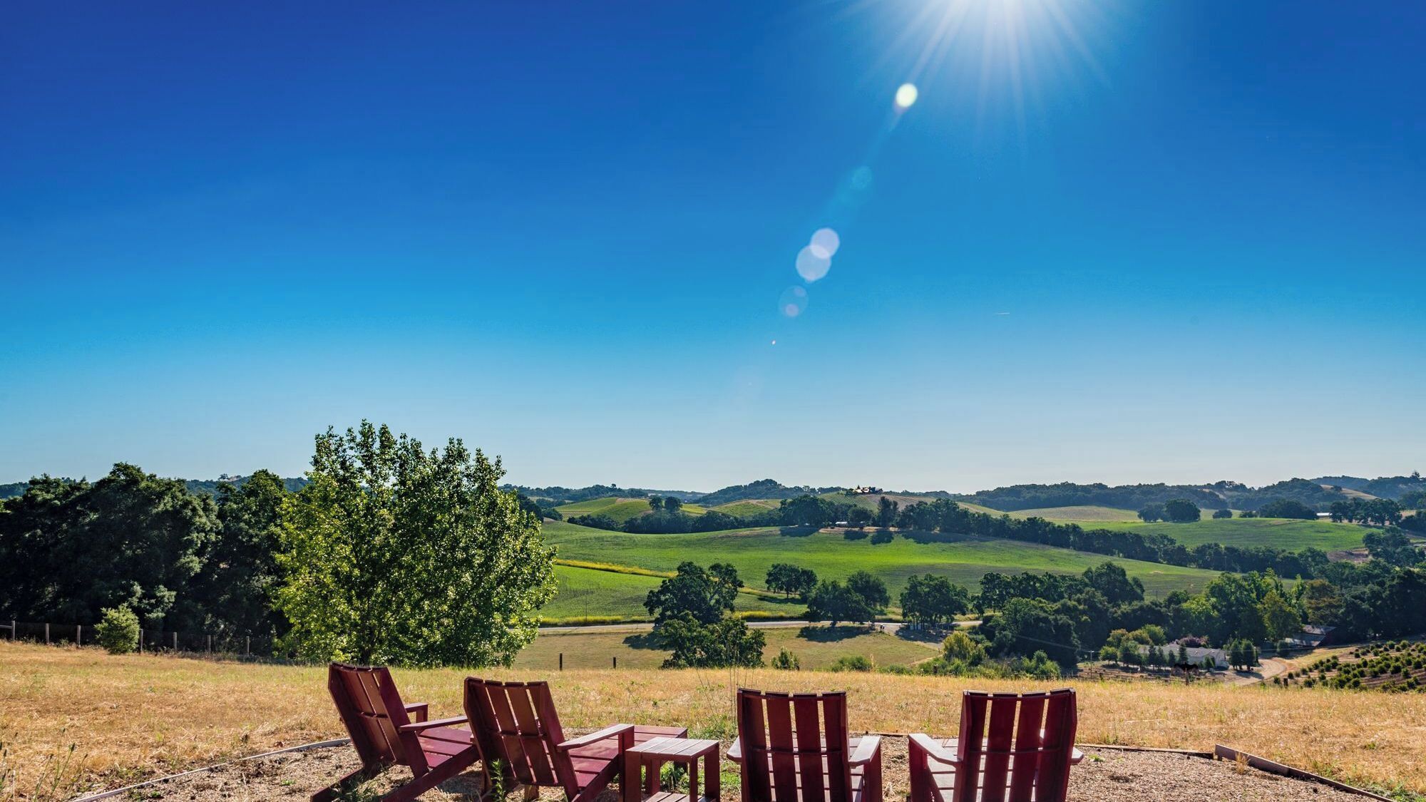 A scenic outdoor seating area with chairs and a table, overlooking rolling hills and a clear blue sky.