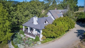 A house with a covered porch, surrounded by dense greenery and a gravel driveway. - Orchard Hill Farm by Avantstay Vineyard Views + Fire Pit + BBQ Countryside Wine Country (Paso Robles)