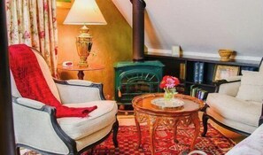 A cozy living room with a fireplace, a red throw on a chair, and a small table with a vase. - Orchard Hill Farm by Avantstay Vineyard Views + Fire Pit + BBQ Countryside Wine Country (Paso Robles)