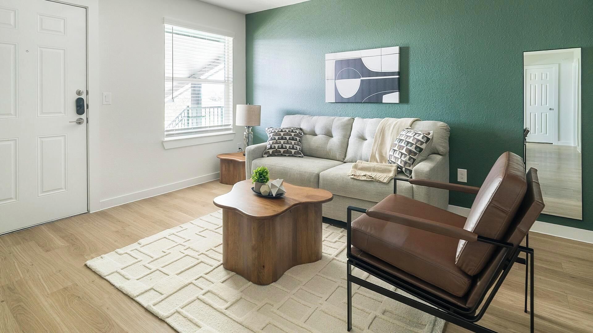 A living room with a sofa, coffee table, and chair. There is a window with blinds, a lamp, and a painting on the wall.