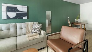 A living room with a sofa, a brown leather chair, a small table with a plant, and a mirror on the wall. - Landing | Beautiful 1BD in Bear Creek (Houston)