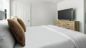 A hotel room with a bed, a television on a wooden dresser, and a white door. - Landing | Chic 1BD in Bear Creek (Houston)