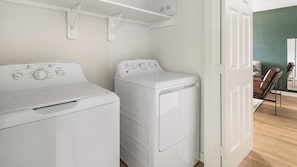 A laundry room with two white washing machines and a shelf above them. - Landing | Chic 1BD in Bear Creek (Houston)