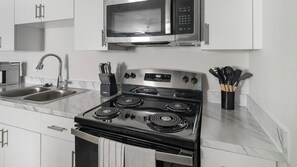 A kitchen with a stainless steel stove, a microwave, a sink, and a utensil holder. - Landing | Chic 1BD in Bear Creek (Houston)