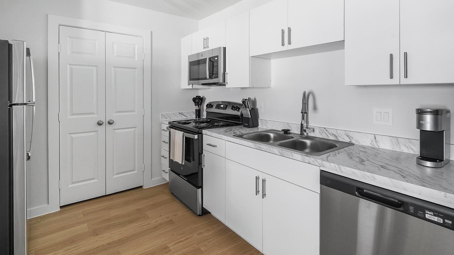 A modern kitchen with white cabinetry, a stainless steel refrigerator, a microwave, a stove, a sink, and a dishwasher.