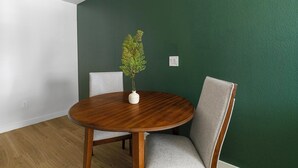 En spiseplads med et rundt træbord, to grå polstrede stole og en hvid vase med en plante.