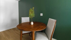 A dining area with a round wooden table, two grey upholstered chairs, and a white vase with a plant. - Landing | Modern 1BD in Bear Creek (Houston)