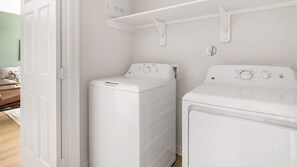 A laundry room with a front-loading washer and dryer, a white door, and a light green wall. - Landing | Stylish 1BD in Bear Creek (Houston)