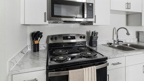 A kitchen with a stove, microwave, sink, and cabinets. - Landing | Modern 1BD in Bear Creek (Houston)