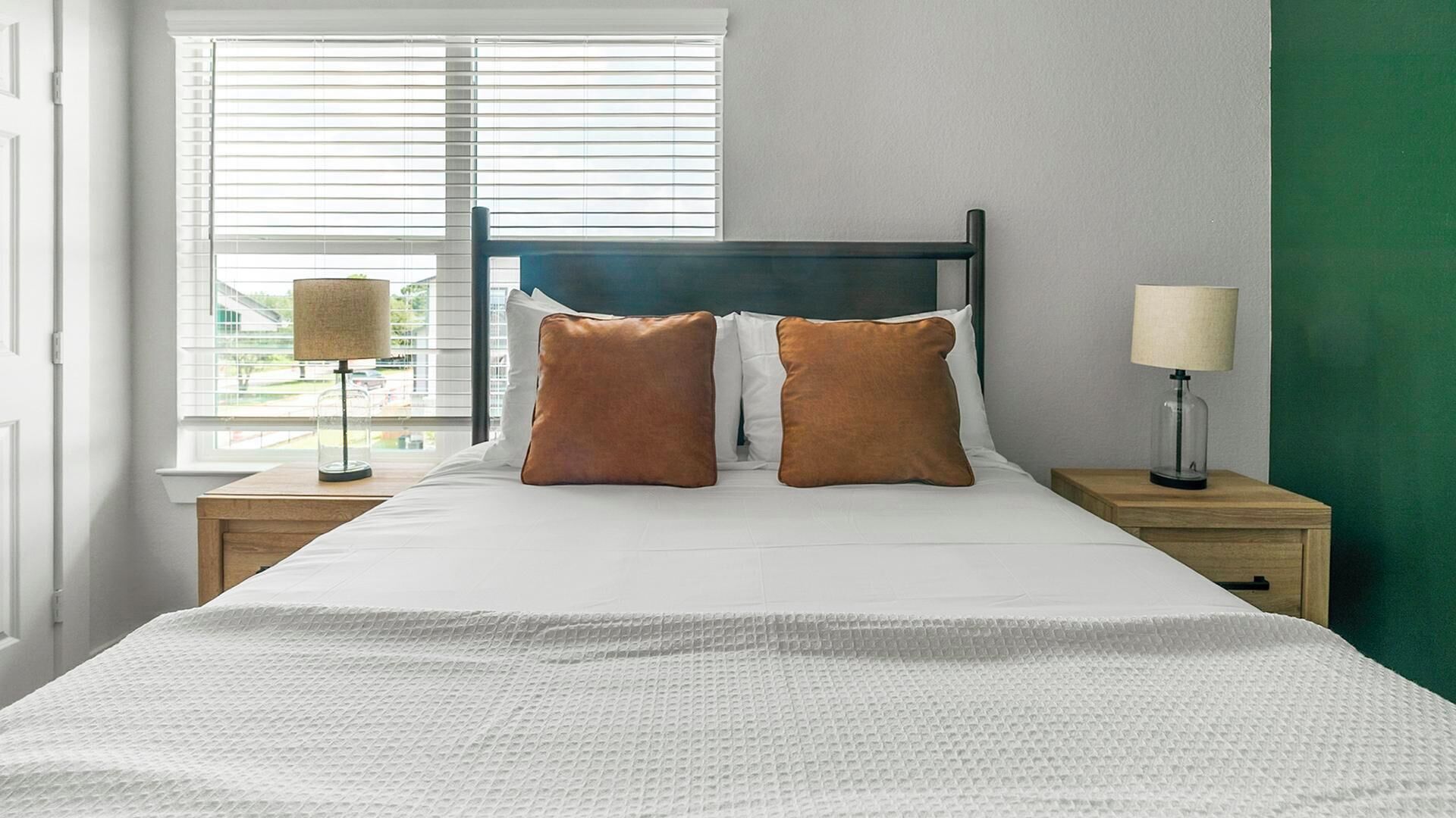 A bedroom with a bed, two nightstands, a lamp, and a window with blinds.
