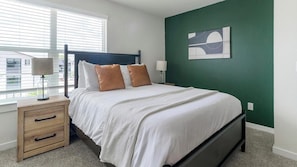 A bedroom with a bed, bedside tables, a lamp, and a window with blinds. - Landing | Modern 1BD in Bear Creek (Houston)