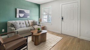 A living room with a sofa, coffee table, and a door. - Landing | Beautiful 1BD in Bear Creek (Houston)