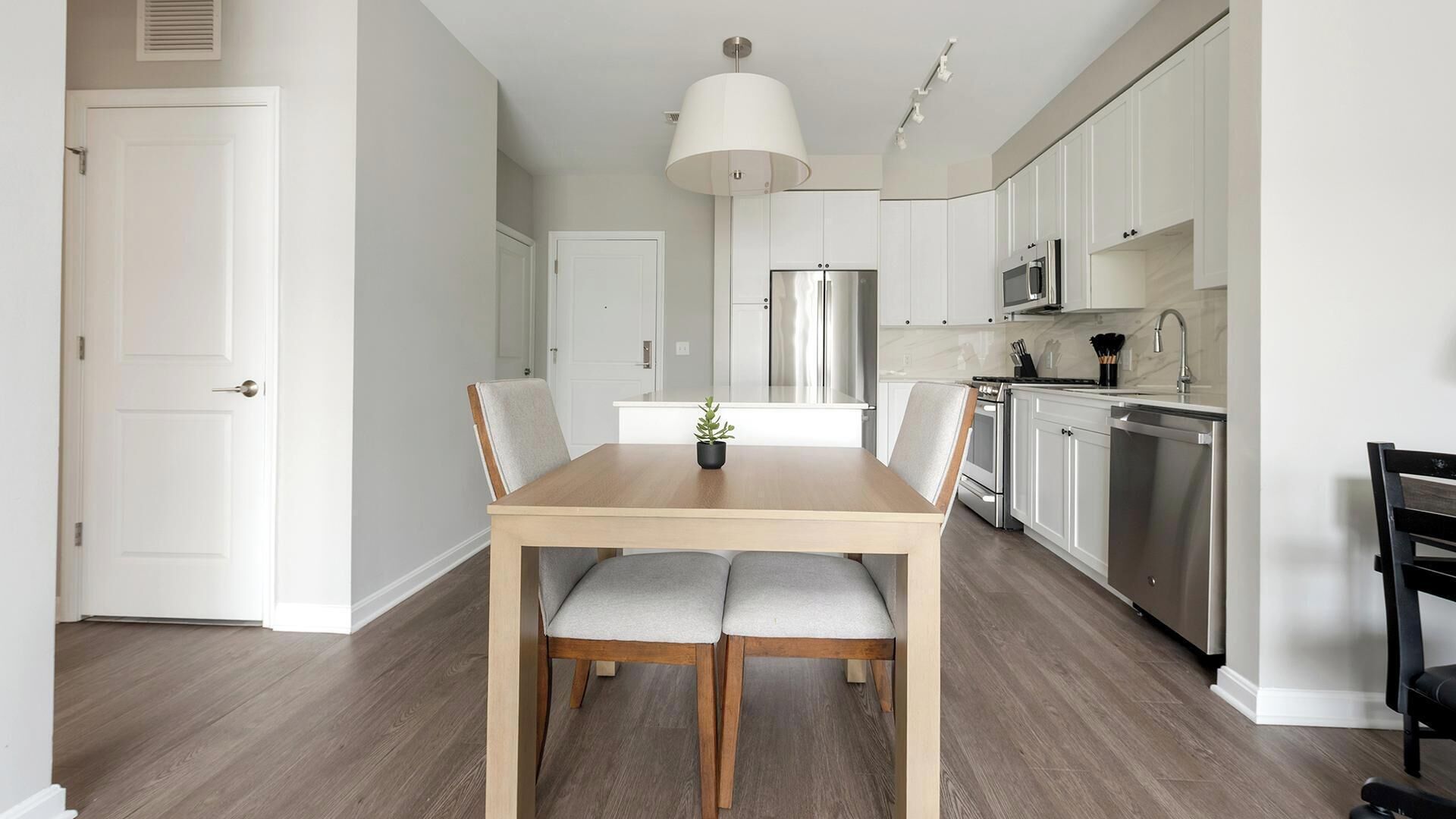 A modern kitchen with white cabinets, stainless steel appliances, and a wooden dining table with grey upholstered chairs.