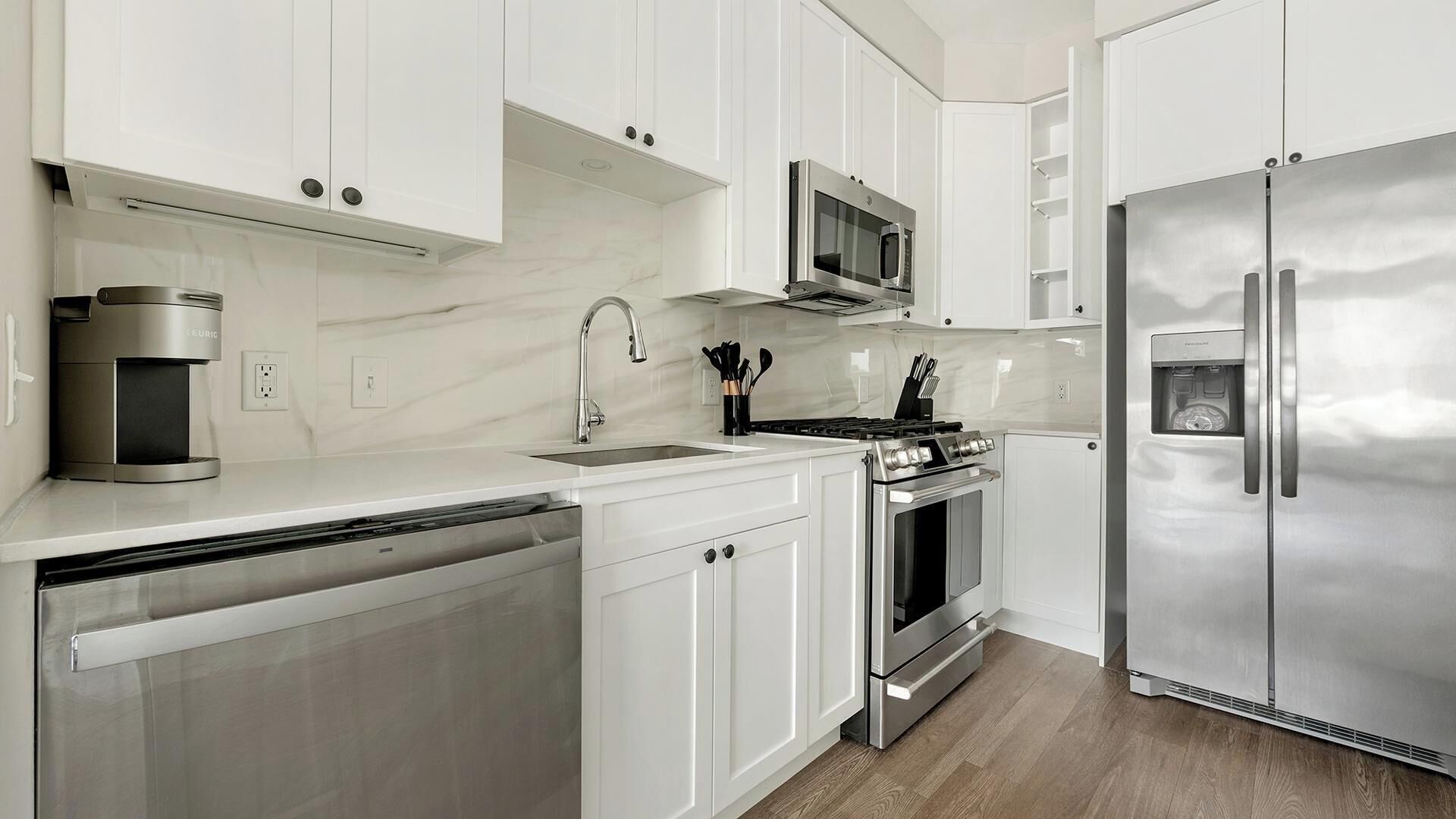A modern kitchen with white cabinetry, stainless steel appliances, a built-in oven, and a dishwasher.