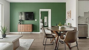 Eine moderne Küche mit grüner Akzentwand, eine Essecke mit rundem Tisch und Stühlen sowie ein sichtbarer Fernseher.