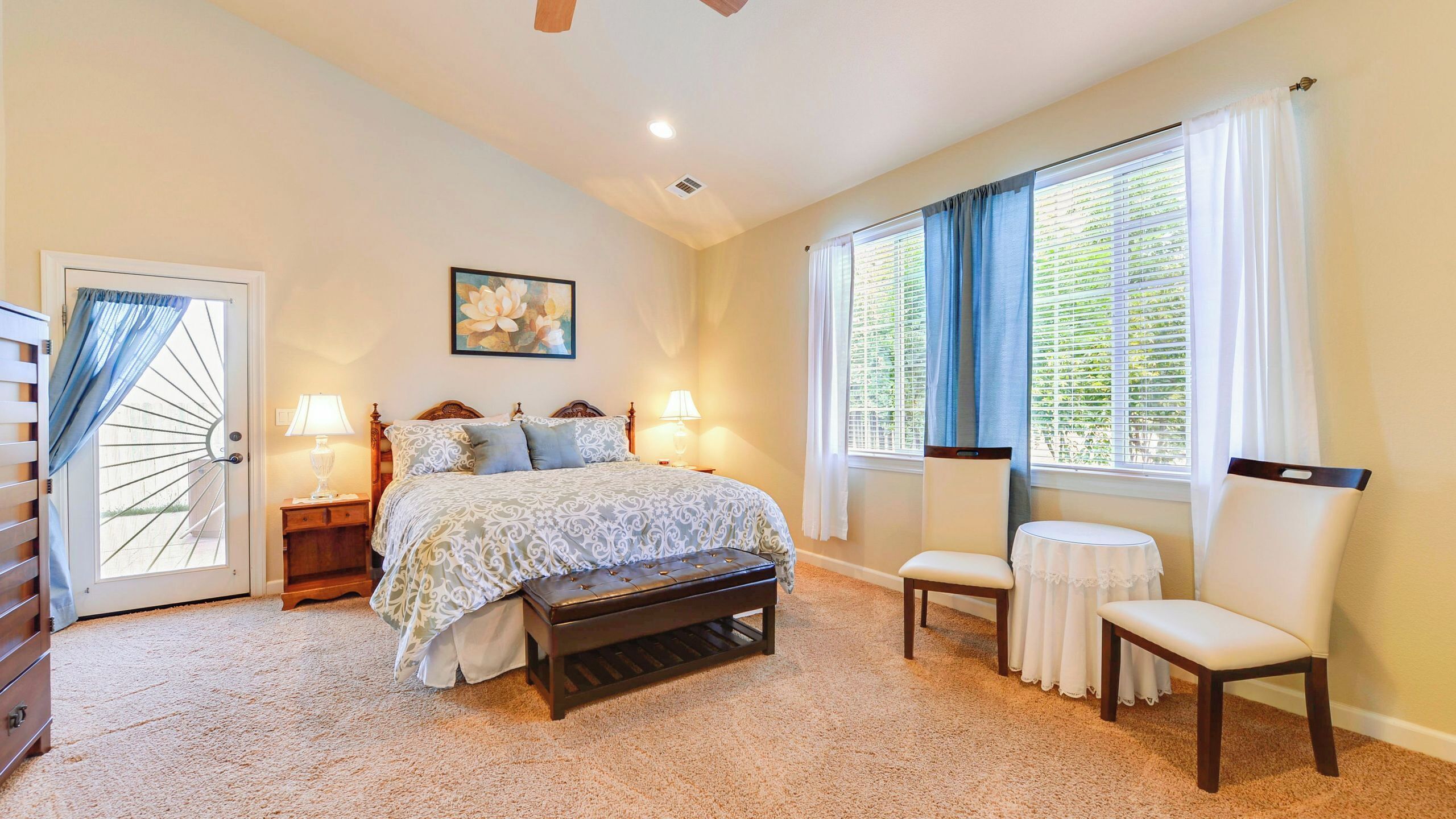 A bedroom with a bed, bench, chair, and two bedside tables with lamps.