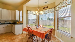 A kitchen with white cabinets, a dining table with orange tablecloth, and a chandelier. - Peace of Mind by Avantstay Fenced BBQ Yard + Game Table Paso Robles (Paso Robles)