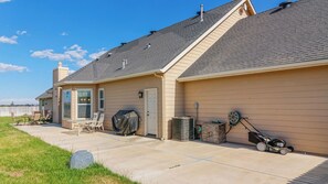 Ein Wohnhaus mit überdachter Terrasse, Grill, Klimaanlage und Rasenmäher.