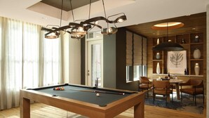 Et billardbord i et rum med moderne design, inklusive et spiseområde med stole og et bord, samt et loft med en unik lampe.