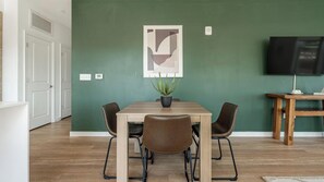 A dining area with a table, chairs, a potted plant, and a painting on the wall. - Landing | Stylish 2BD, Gym, Rooftop Lounge (Chevy Chase)