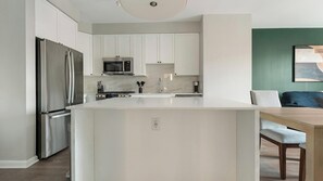A modern kitchen with white cabinetry, stainless steel appliances, and a central island. - Landing | Spectacular 1BD, Gym, Rooftop Lounge (Chevy Chase)
