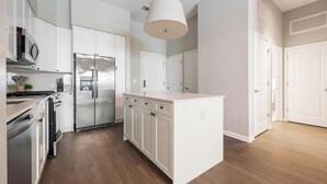 A modern kitchen with stainless steel appliances, white cabinetry, and a central island. - Landing | Spectacular 1BD, Gym, Rooftop Lounge (Chevy Chase)
