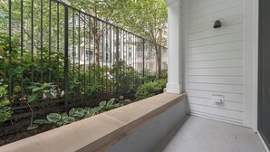 A concrete planter with plants, a metal fence, and a white building with a window. - Landing | Spectacular 1BD, Gym, Rooftop Lounge (Chevy Chase)