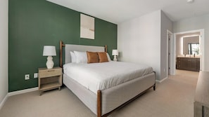 A bedroom with a bed, bedside tables, and a view into the bathroom. - Landing | Modern 2BD, Gym, Rooftop Lounge (Chevy Chase)
