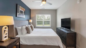 Un dormitorio con cama, televisor, ventilador de techo y ventana con persianas.