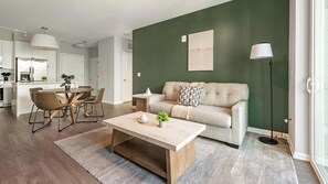 A modern living room with a sofa, coffee table, and dining area. - Landing | Modern 2BD, Gym, Rooftop Lounge (Chevy Chase)